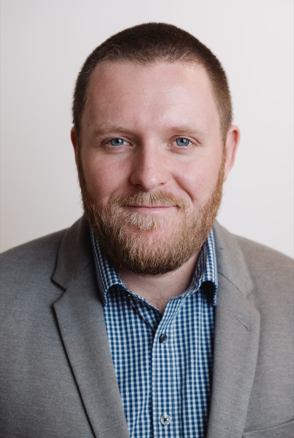 Professional headshot of a bearded man in a grey suit and checked shirt