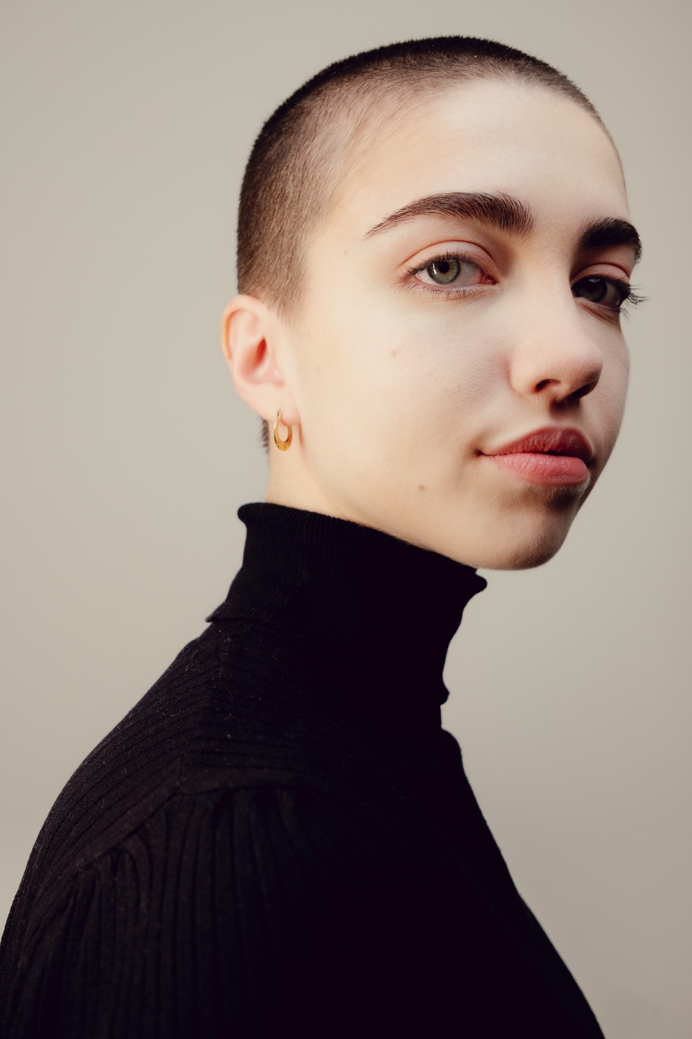 Colour studio portrait of a model with a shaved head and gold hoop earring