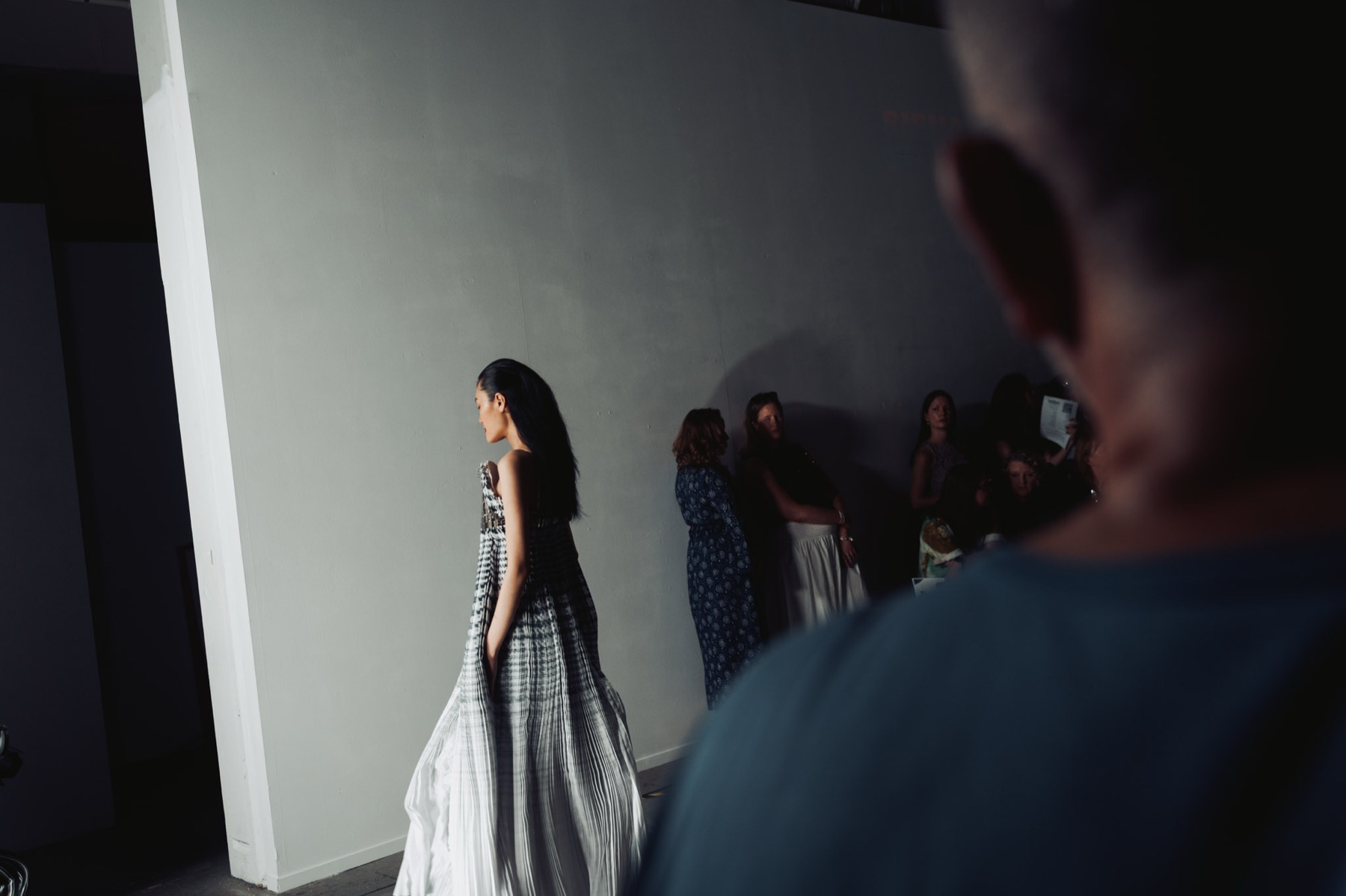 Fashion showcase model in a pleated gown crossing a lit wall